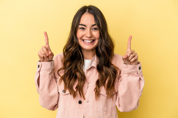 Young caucasian woman isolated on yellow background indicates with both fore fingers up showing a...
