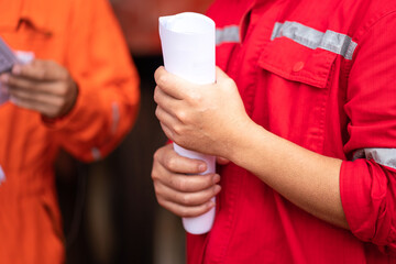 An operational staff is holding a rolled paper document during group meeting in safety audit and inspection activity. Indsutrial action photo. Close-up and selective focus at people hand.