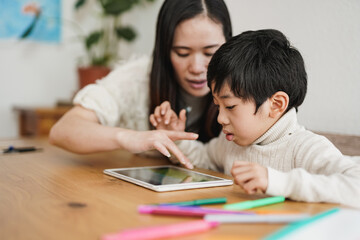 Asian nanny and preschool child learning with digital tablet indoor - Daycare and technology concept