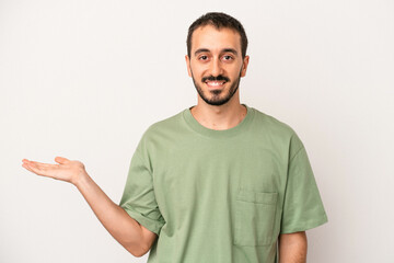 Young caucasian man isolated on white background showing a copy space on a palm and holding another...