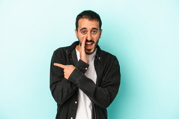 Young caucasian man isolated on blue background saying a gossip, pointing to side reporting something.