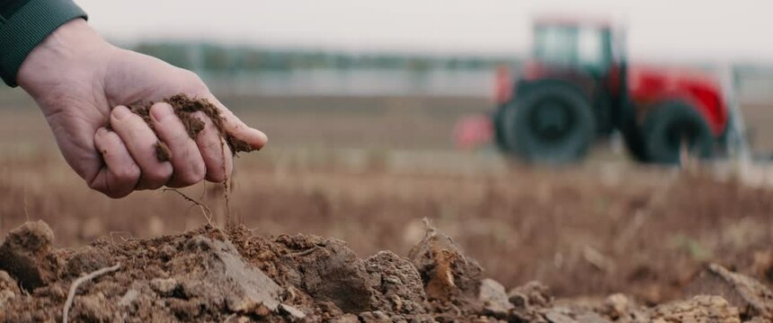 CU on hands, Caucasian male farmer picking up soil, tractor in the background. Shot with 2x anamorphic lens