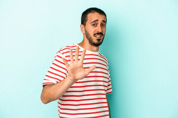Young caucasian man isolated on blue background being shocked due to an imminent danger