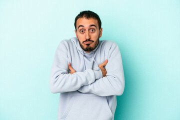 Young caucasian man isolated on blue background shrugs shoulders and open eyes confused.