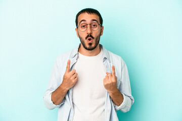 Young caucasian man isolated on blue background pointing upside with opened mouth.