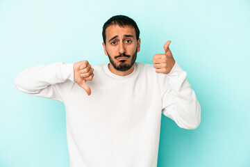 Young caucasian man isolated on blue background showing thumbs up and thumbs down, difficult choose...