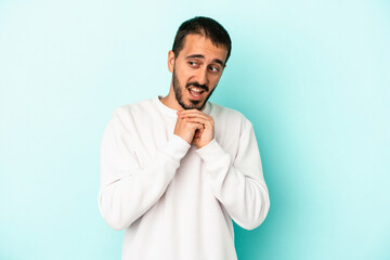 Young caucasian man isolated on blue background praying for luck, amazed and opening mouth looking to front.