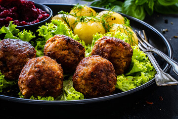 Roast meatballs with boiled potatoes, beetroots and fresh green vegetables on wooden black table
