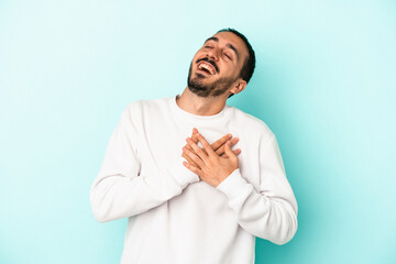 Young caucasian man isolated on blue background laughing keeping hands on heart, concept of happiness.