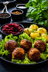 Roast meatballs with boiled potatoes, beetroots and fresh green vegetables on wooden black table
