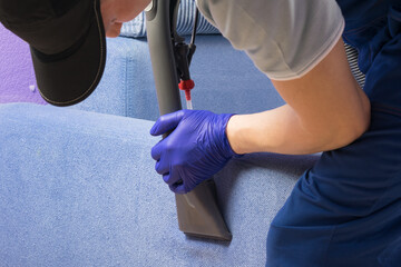 vacuum cleaner brush picks up foam from blue sofa, cleaning company employee, top view