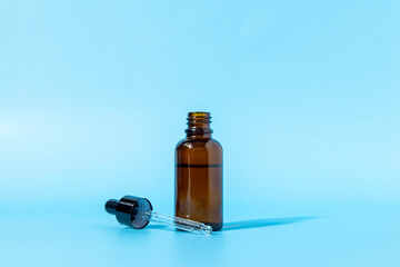 Glass dropper bottle made of brown glass on a blue background casts a shadow. Front view with copy space. Mockup of a cosmetic product. Serum for skin care.