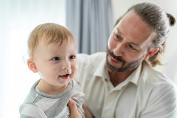 Caucasian loving father holding baby boy child in house living room. 