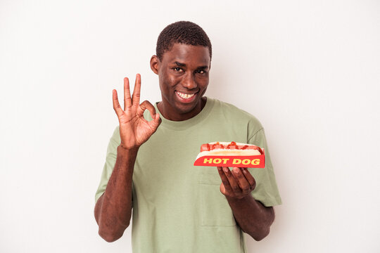 Young African American Man Eating A Hot Dog Isolated On White Background Cheerful And Confident Showing Ok Gesture.