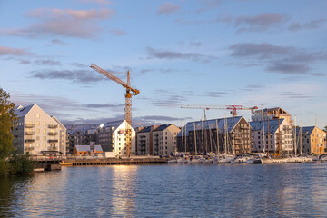 A view of appartment buildings being built near the lake with boats and yacht in the front. - obrazy, fototapety, plakaty