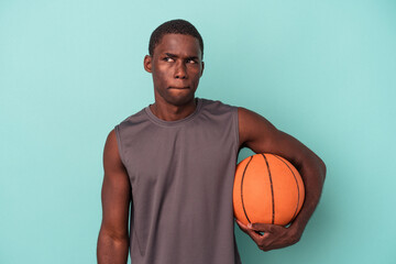 Young African American man playing basketball isolated on blue background confused, feels doubtful and unsure.