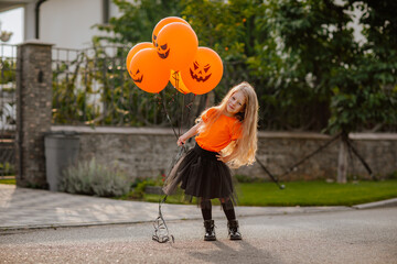 Girl playing on the street with pumpkin balloons while sunrise.