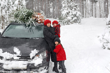 A happy mother with her daughter next to a Christmas tree from the market, loaded onto the roof of a black car. Preparation for the celebration of New Year and Christmas. Family Winter holidays