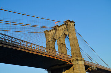 A close-up of the Brooklyn Bridge with the American flag on the top seen from Frankfort Street in...