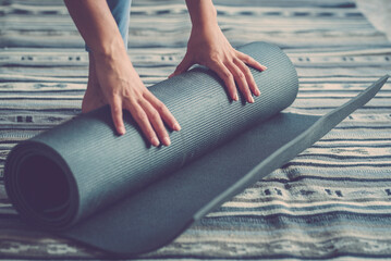 Healthy fitness woman hands rolling up mat after exercise on floor in living room, Woman doing exercise at home. Hands of woman rolling or unrolling yoga mat on floor at home
