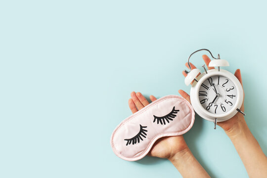 Sleep concept with mask, woman hand and alarm on blue background