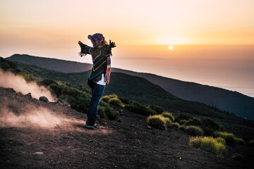 Carefree woman in warm clothing with her arms outstretched on mountain slope admiring scenic view of sunset. Female hiker exploring nature on vacation