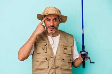 Fototapeta premium Middle age caucasian fisherman holding rod isolated on blue background showing a disappointment gesture with forefinger.