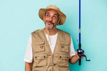 Middle age caucasian fisherman holding rod isolated on blue background  dreaming of achieving goals and purposes