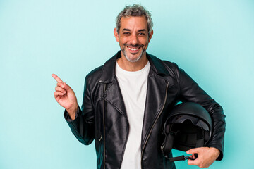 Middle age biker caucasian man holding helmet isolated on blue background  smiling and pointing...