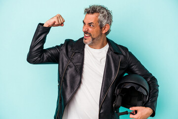 Middle age biker caucasian man holding helmet isolated on blue background  raising fist after a...