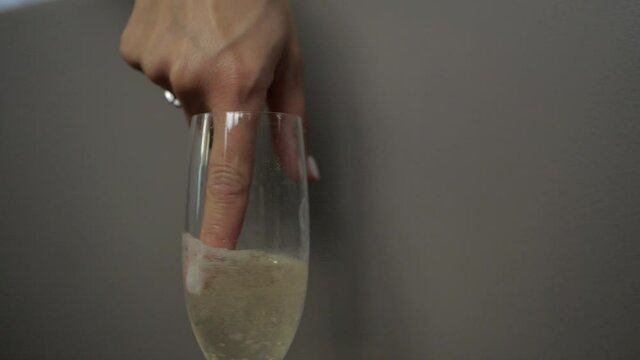a beautiful woman stirs champagne in a glass with her finger, erotically licks her finger and looks directly into the camera. High quality FullHD footage