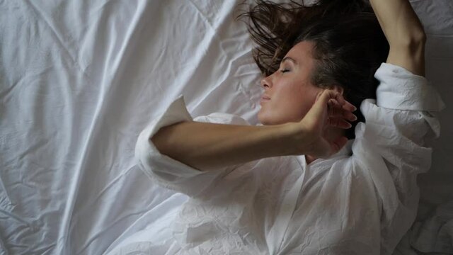 sexy woman brunette dancing with her hands lying on white bed linen. High quality FullHD footage