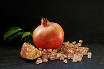 Ripe pomegranate with green leaves, a segment of pomegranate and grains on a black background....