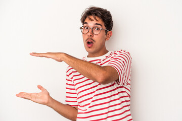 Young mixed race man isolated on white background holding something with both hands, product presentation.