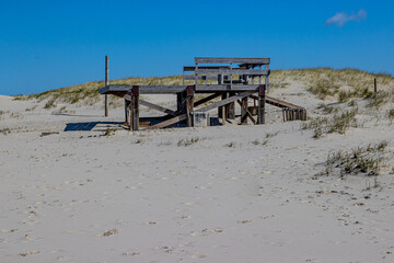Fototapeta na wymiar Beach with an old abandoned wooden structure with a small hill with brown grass in the background, sunny day with a blue sky in Petten aan Zee, Noord-Holland in Nederland
