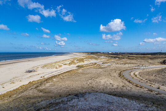 Marram grass over the dunes, a country road, empty beach with the sea and the horizon in the background, sunny spring day with a blue sky and clouds in Petten aan Zee, Noord-Holland in the Netherlands © Emile