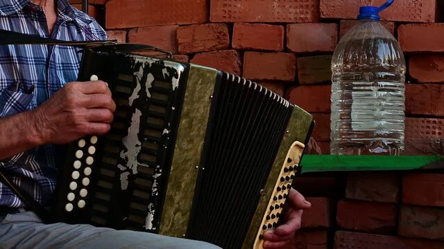 Senior man playing with an old accordion outdoor stage sitting on chair.