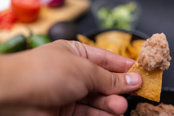 Hand holding tortilla chip with refried beans above blurry vegetables