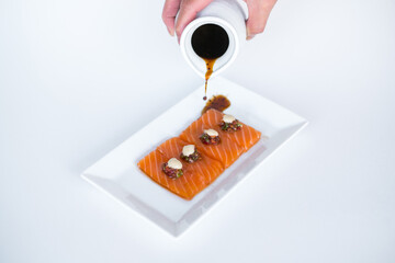 Hand pouring soy sauce on Salmon sashimi on white plate on white background. Isolated on white. Japanese traditional food. Healthy food concept.