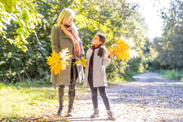 Fashionable mother with daughter. Family in a autumn park. Little daughter in a coat.