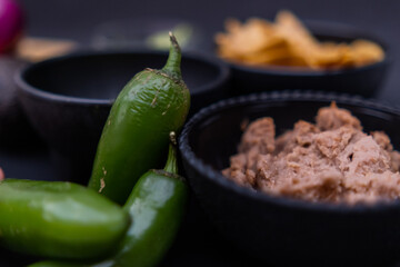 Chili peppers leaning against bowls of tortilla chips and refried beans