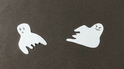 Halloween. Two white paper ghosts on a black paper surface.