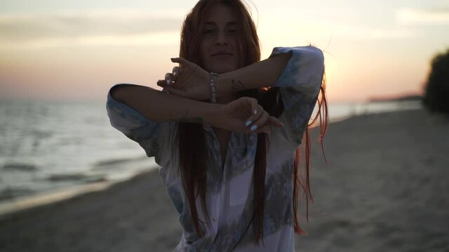 Beautiful young brunette posing at the camera on the background of the sea. Portrait of a woman on sandy beach at sunset