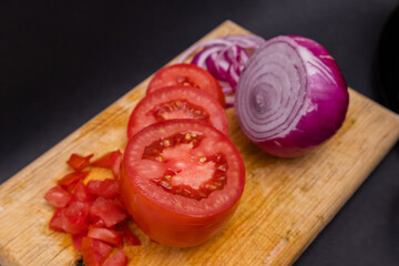 Sliced tomato and onion on cutting board above black surface