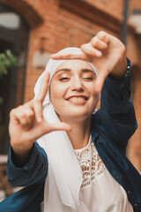 Portrait of young muslim girl making a camera frame with fingers outdoors.