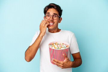 Young mixed race man eating popcorns isolated on blue background biting fingernails, nervous and very anxious.