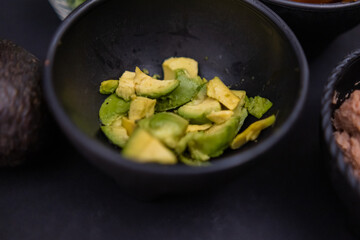Small bowl of chopped avocado on black surface