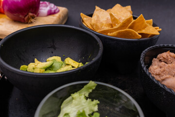 Sliced vegetables and bowls of tortilla chips and beans with black background