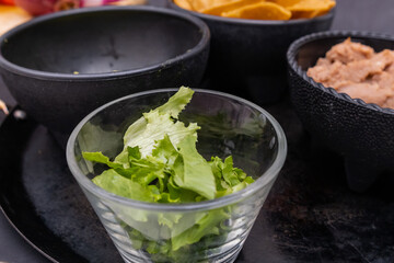 Bowls of chopped lettuce, tortilla chips, and refried beans on Mexican comal