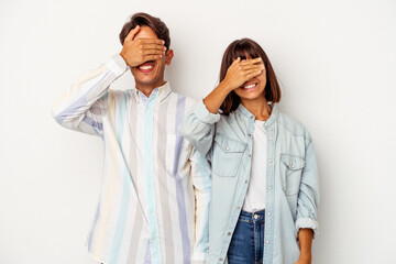 Young mixed race couple isolated on white background covers eyes with hands, smiles broadly waiting for a surprise.